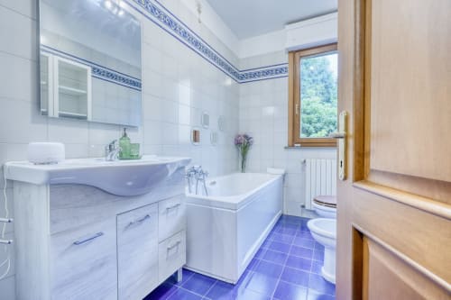 Moderno bagno della luxury B&B SleepWithMe a Pisa con pavimento in piastrelle blu, vanity bianca, vasca da bagno e finestra con vista sul giardino
