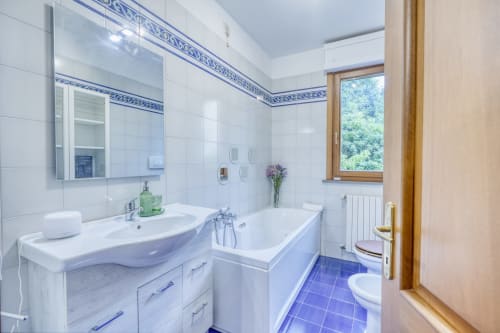 Lussuoso bagno moderno presso il B&B SleepWithMe di Pisa con piastrelle bianche, dettagli blu, lavabo, vasca e vista sul giardino