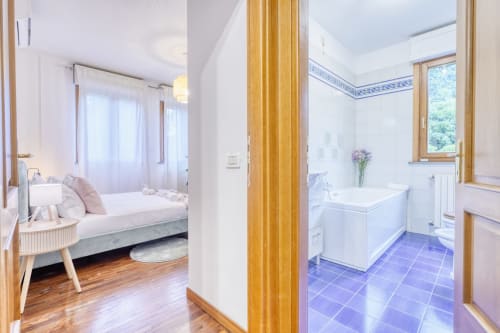 Camera da letto e bagno moderni presso il SleepWithMe Luxury B&B a Pisa, con letto bianco, bagno con piastrelle blu e vista sul giardino