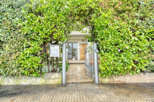 Ingresso recintato dell'Evergreen Luxury B&B a Pisa, circondato da rigogliosa edera e fiori rampicanti che conducono al suggestivo cottage