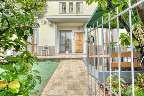Ingresso della corte fiorita dell'appartamento Evergreen Luxury B&B a Pisa con sentiero lastricato e tenda verde
