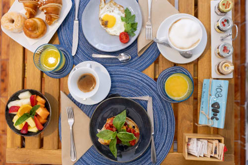 Colazione a Villa Bina Sea Hotel con dolcetti, uova, frutta fresca, succhi e caffè su tavolo in legno.