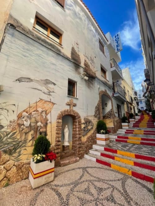 Calle escalonada colorida con mural religioso en Hotel Boutique Galeón de Calpe, España