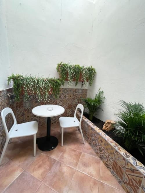 Acogedor patio exterior del Hotel Boutique Galeon Calpe con sillas blancas, mesita y plantas colgantes exuberantes sobre muros blancos