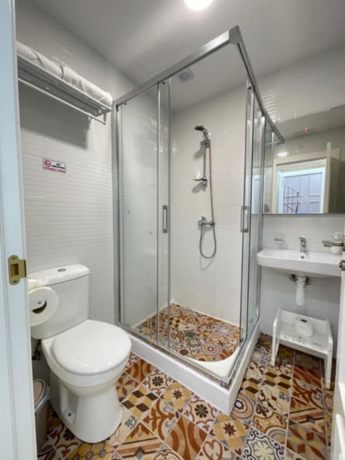 Baño moderno en Hotel Boutique Galeon Calpe con azulejos metro blancos, ducha abierta, inodoro, lavamanos y detalles decorativos