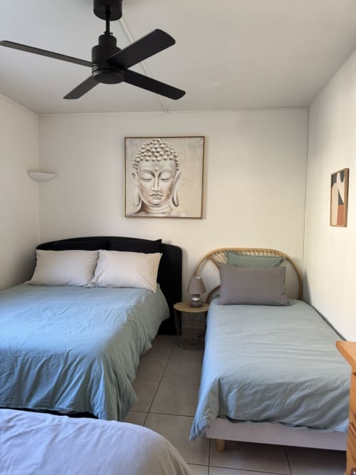 Chambre Bodhi à L'instant D'un Séjour, Le Gua : lits jumeaux avec draps bleus, ventilateur au plafond noir, œuvres bouddhistes, fauteuil en rotin