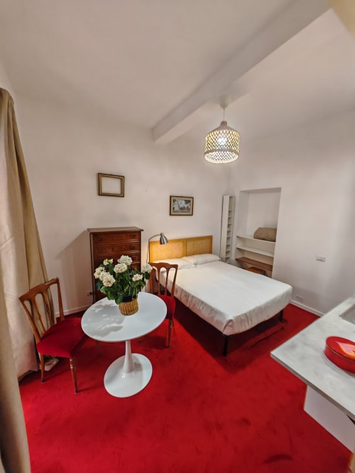 Camera da letto romana elegante con moquette rossa, letto in legno, tavolino rotondo bianco e lampada a sospensione in ottone