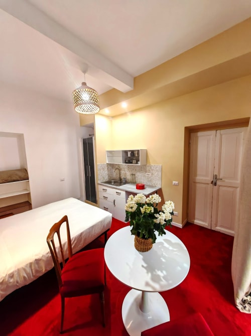 Moderno studio con moquette rossa, angolo cottura, tavolo rotondo bianco con fiori presso Roman Forum Flat, Roma