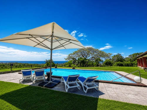 Luxury villa pool with ocean view, lounge chairs under umbrella at ILMO Conciergerie, Le Gosier