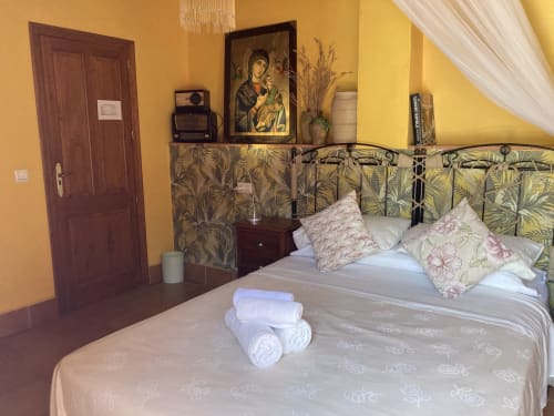 Cozy bedroom at Casa Gallinera vacation home in Alicante with yellow walls, ornate headboard, and mountain views
