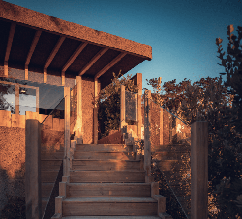 Terraço Charm Nature B&B em Azóia com escadas de madeira, paredes de cortiça e céu azul na hora dourada