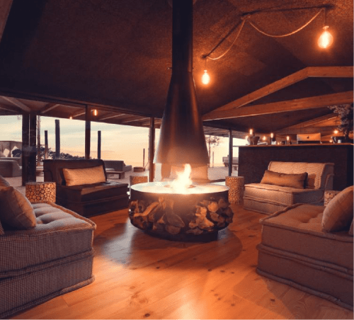 Sala de estar luxuosa com lareira central na pousada Charm Nature em Azóia, Portugal, com iluminação ambiente e vista panorâmica