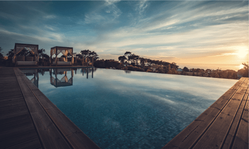 Piscina infinita do Charm Nature BnB ao pôr do sol com vista para Azóia, Portugal e deck de madeira