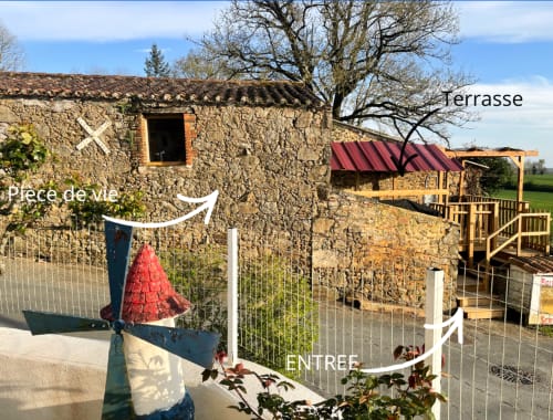 Entrée du Petit Moulin BnB avec bâtiment en pierre, terrasse et pergola rouge à Pouzauges