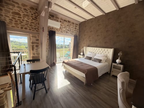 Chambre double luxueuse avec tête de lit matelassée crème, murs en pierre, puits de lumière et balcon vue campagne aux Instants