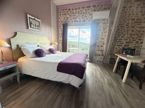 Élégante chambre double aux Instants Volés avec accents violets, murs en pierre, balcon vue jardin et équipements modernes