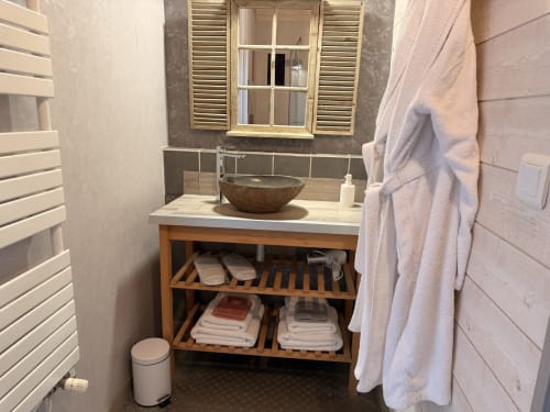 Vasque en pierre ronde, étagères en bois et serviettes blanches dans la salle de bains moderne de l'hôtel-boutique Les Instants Volés