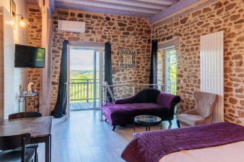 Chambre glamour spacieuse aux Instants Volés avec murs en pierre, méridienne violette, TV et balcon avec vue sur le jardin