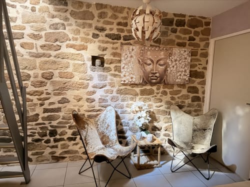 Coin détente aux murs en pierre des Instants Volés avec fauteuils papillon, œuvre Bouddha et décoration rustique