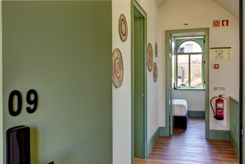 Hallway in Sintra Green Chalet B&B with room 09, decorative woven plates, green doors, and fire extinguisher