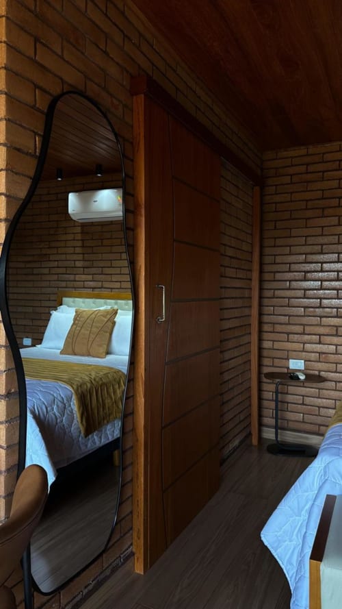 Quarto da villa Vivendas Canaã com espelho arqueado, móveis em madeira, paredes de tijolos e vista para a montanha