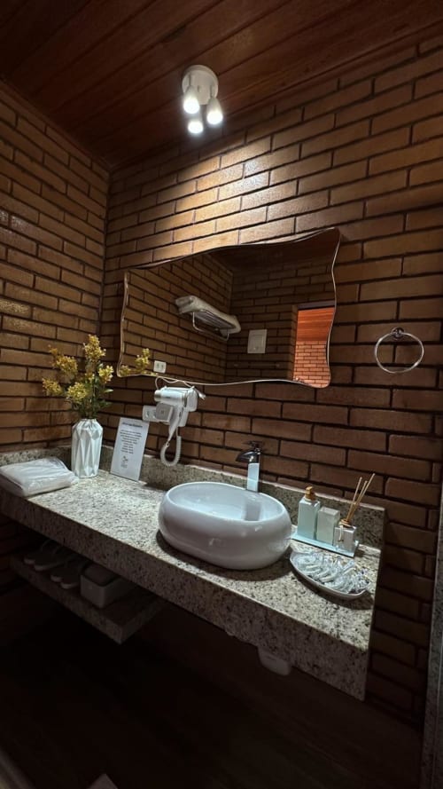 Banheiro moderno na vila Vivendas Canaã com cuba de vidro, paredes de tijolos, espelho e amenidades em Espera Feliz