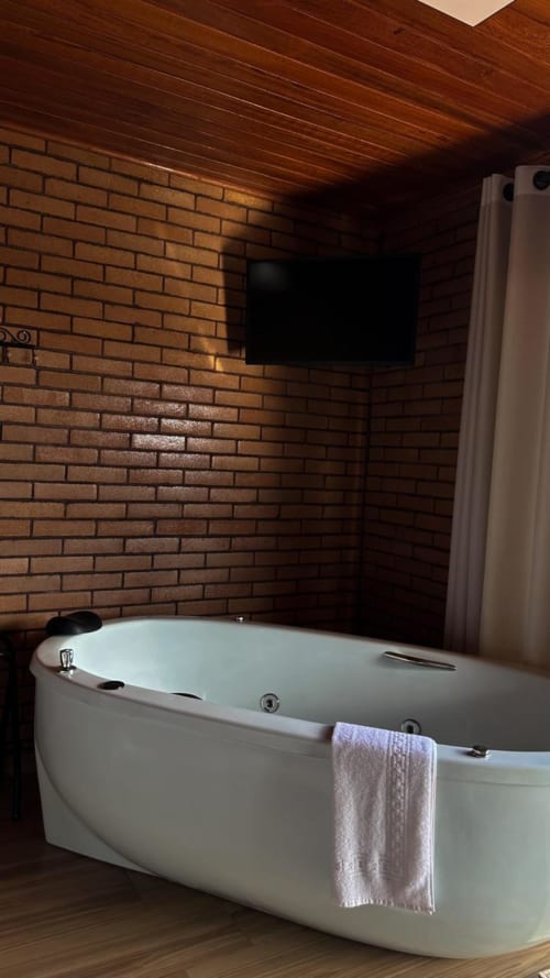 Banheira de luxo em spa com toalha em banheiro com parede de tijolos na villa Vivendas Canaã, TV acima