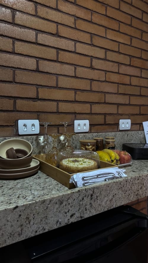 Bancada de cozinha com tampo de granito, tomadas brancas, tigelas, copos, frutas frescas e pão na villa Vivendas Canaã em Espera