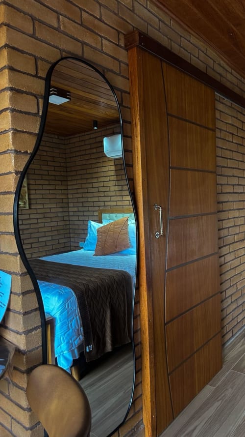 Quarto moderno da villa Vivendas Canaã com roupas de cama azuis, espelho arqueado, porta de madeira e paredes de tijolos