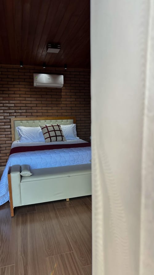 Quarto moderno na vila Vivendas Canaã com roupa de cama azul, parede de tijolos, teto de madeira escura e ar condicionado de parede