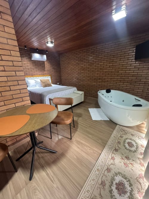 Suíte Hibisco da villa Chalé com cama, mesa de jantar e banheira jacuzzi branca em Vivendas Canaã, Espera Feliz