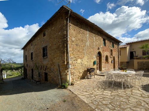 Stone Tuscan villa exterior with courtyard seating at Tuscan Sun Stays, Lajatico Italy, sunny mountain views