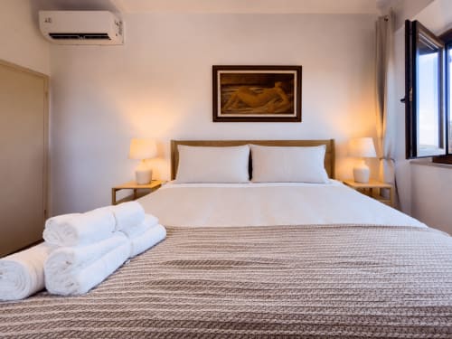 Serena apartment bedroom at Tuscan Sun Stays with white bedding, wooden bed frame, twin lamps, and mountain views in Lajatico
