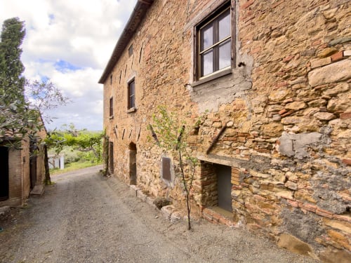 Rustic stone exterior of Tuscan Sun Stays apartment in Lajatico, Italy, with mountain views and ivy-covered walls