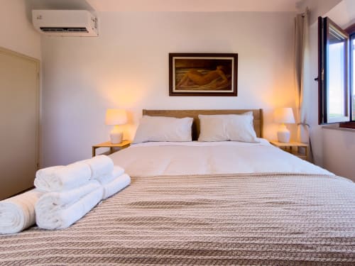 Serena apartment bedroom at Tuscan Sun Stays with wooden bed, white linens, rolled towels, bedside lamps, and mountain views