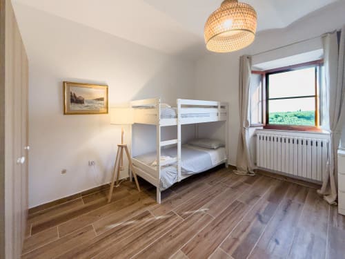 Bright bedroom in Tuscan Sun Stays with white bunk beds, wooden floors, woven ceiling lamp, mountain views, and modern