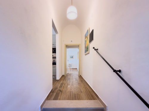 Modern hallway in Tuscan Sun Stays apartment with wooden floors, white walls, pendant light, and staircase railing