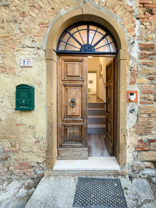 Tuscan stone building entrance with wooden door, transom window, and green mailbox at Tuscan Sun Stays in Lajatico, Italy