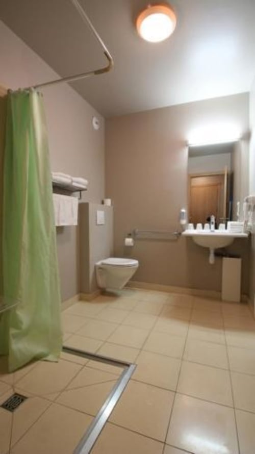 Salle de bain accessible et moderne à l'hôtel Les Balcons du Sancy, avec rideau de douche vert, lavabo, toilettes et luminosité généreuse