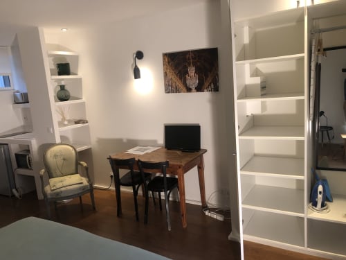 Studio moderne chez Denis & Virginie à Versailles avec bureau, chaise, table en bois, TV et étagères blanches