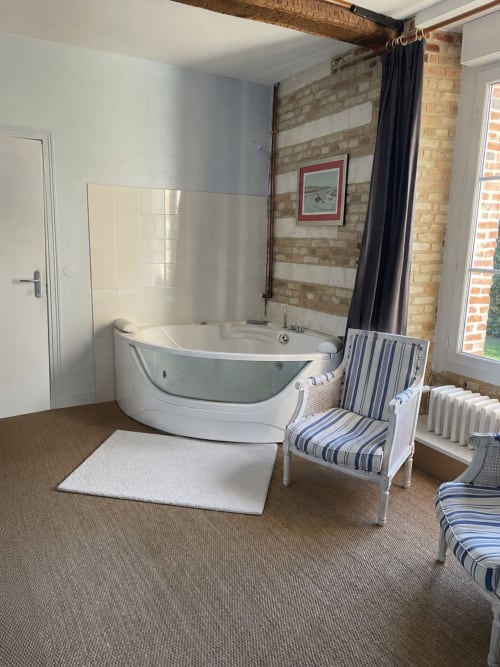 Suite salle de bain spa luxe à la Maison Nolette B&B avec baignoire jacuzzi blanche, murs en brique apparente et vue sur jardin