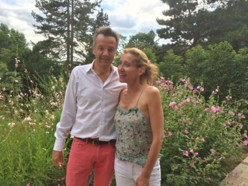 Couple souriant dans le jardin fleuri du gîte Denis & Virginie à Versailles, entouré de fleurs roses et d'arbres