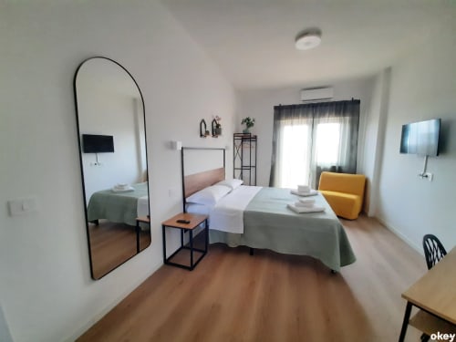 Camera moderna al B&B Bari Centro con letti singoli gemelli, specchio ad arco, sedia gialla, TV e balcone con vista sulla città a Bari, Italia