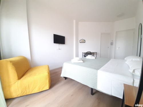 Camera luminosa con sedia gialla, due letti con lenzuola bianche, TV a muro e pavimenti in legno al B&B Bari Centro