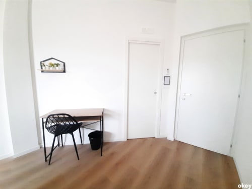 Camera minimal al B&B Bari Centro con pavimento in legno, sedia nera, tavolino, pareti bianche e più porte