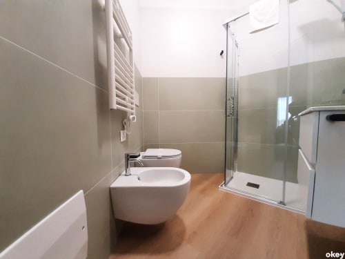 Bagno moderno in hotel a Bari con bidet, WC, lavabo bianco, scaldarottoli, box doccia in vetro e pavimento in legno
