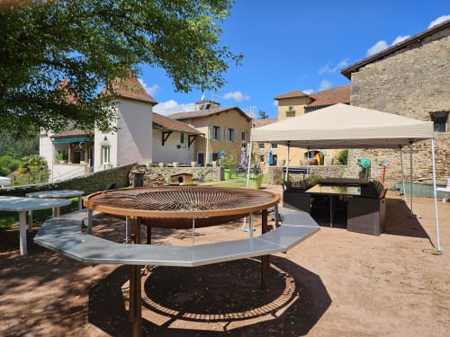 Cour extérieure des Gîtes Les Muriers avec sièges circulaires en bois, tables, parasol crème et bâtiments en pierre