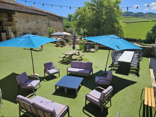 Salon de jardin extérieur aux Gites Les Muriers, Bourgvilain avec parasols bleus, assises violettes et pelouse verdoyante
