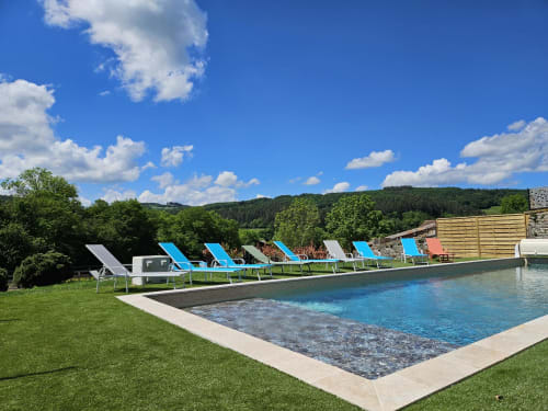 Piscine avec transats bleus aux Gîtes Les Muriers à Bourgvilain, entourée de pelouses verdoyantes et de collines boisées