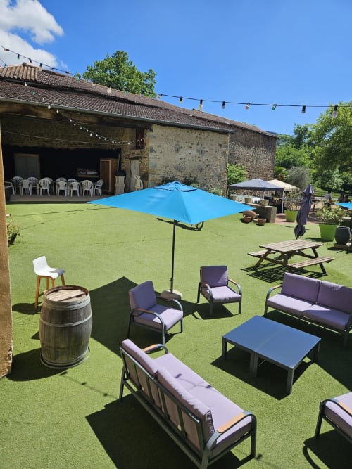 Salon de jardin extérieur aux Gîtes Les Muriers avec parasol bleu, espaces de détente et chaumière en pierre à Bourgvilain